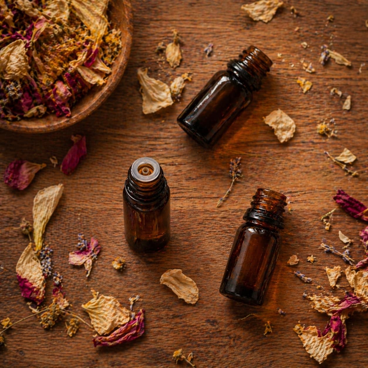 Amber essential oil bottles arranged with dried flower petals on a wooden board